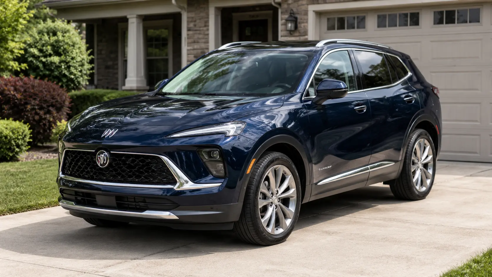 A dark blue 2026 Buick Envision crossover parked in a suburban driveway in daylight, shot candidly at a three-quarter angle.
