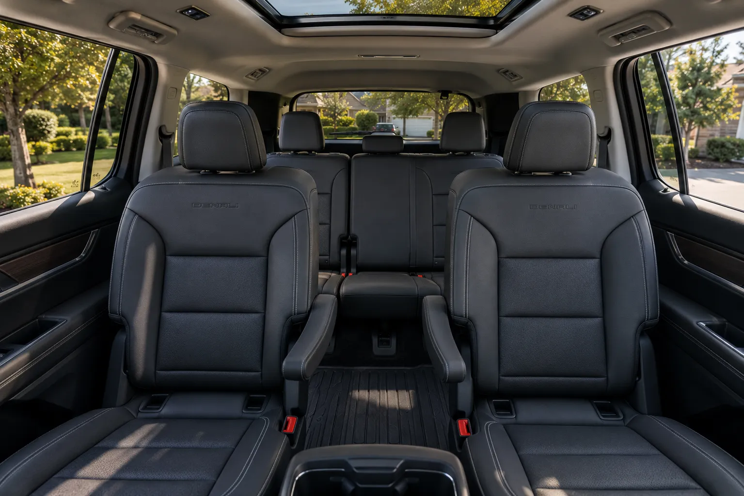 The three-row interior of a GMC Acadia, lit by natural daylight through the panoramic sunroof.