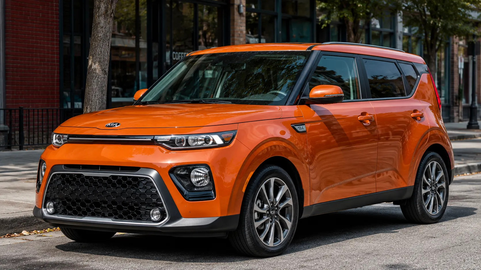 An orange Kia Soul subcompact SUV parked on a city street in daylight, shot candidly at a three-quarter angle.