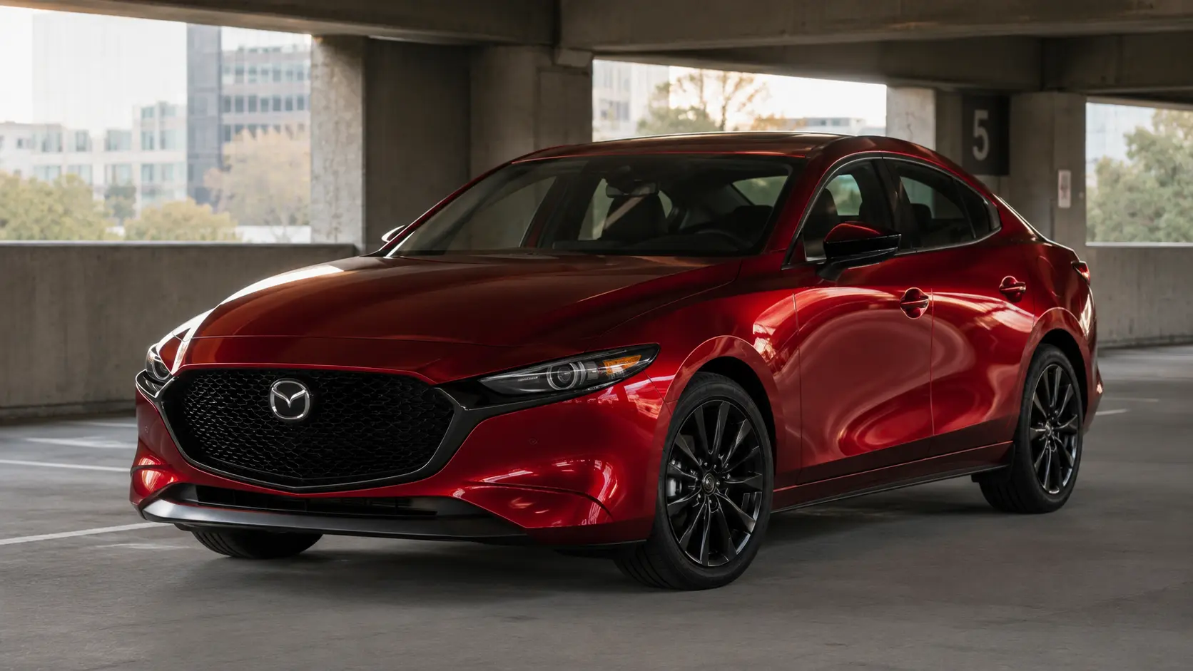 A red 2026 Mazda3 sedan parked in a parking garage under natural ambient light, shot candidly at a three-quarter angle.