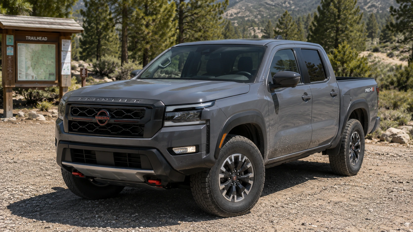 A gray 2026 Nissan Frontier pickup truck parked at a trailhead in daylight, shot candidly at a three-quarter angle.