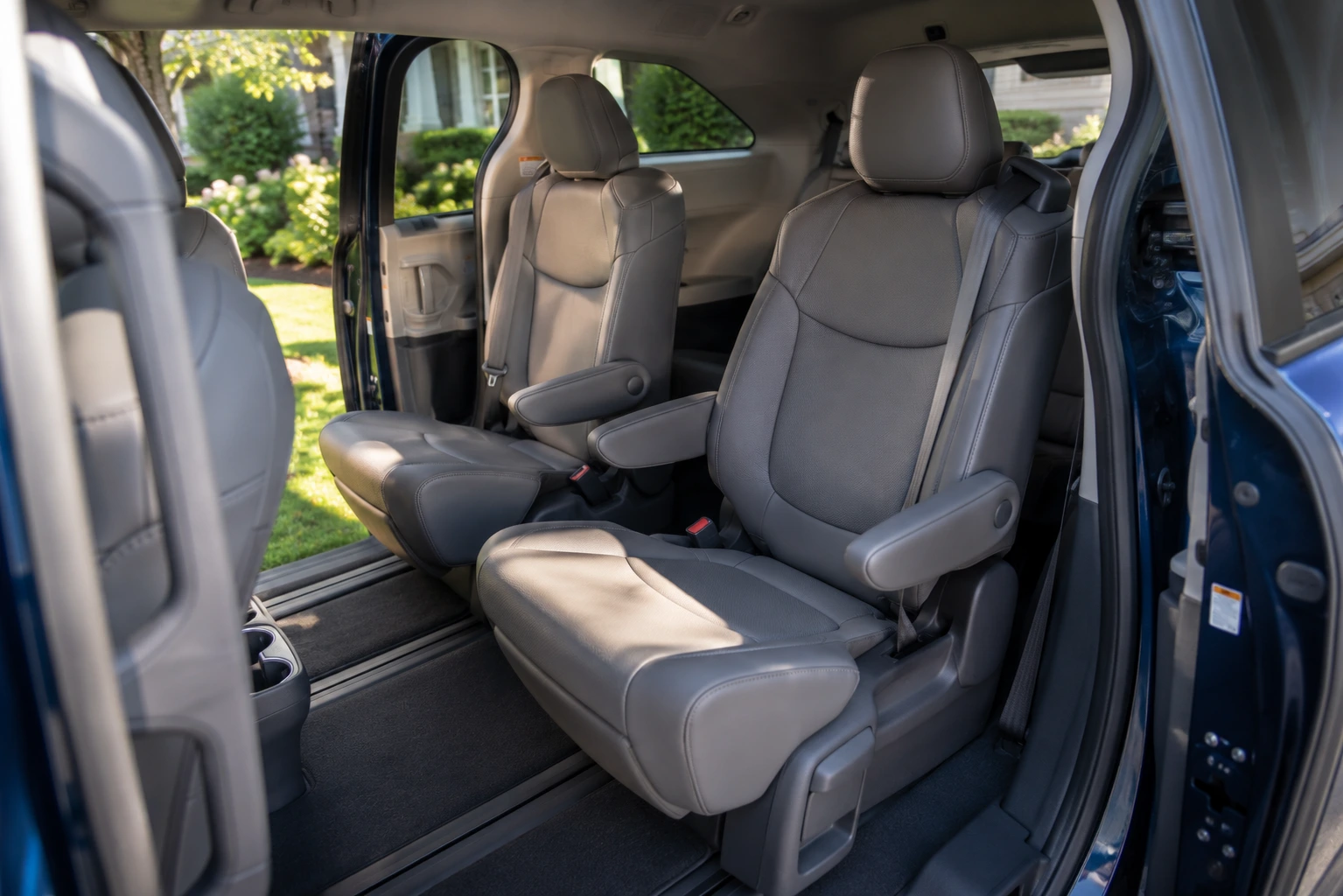 The spacious second-row captain's chairs and sliding door interior of a Toyota Sienna, lit by natural daylight.